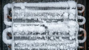 Macro photograph capturing a completely frozen HVAC evaporator coil. A thick layer of white hoarfrost and dense ice covers the aluminum fins and copper tubing, creating a blocked airflow failure state. Individual ice crystals and delicate formations are sharply in focus. High detailed textures.